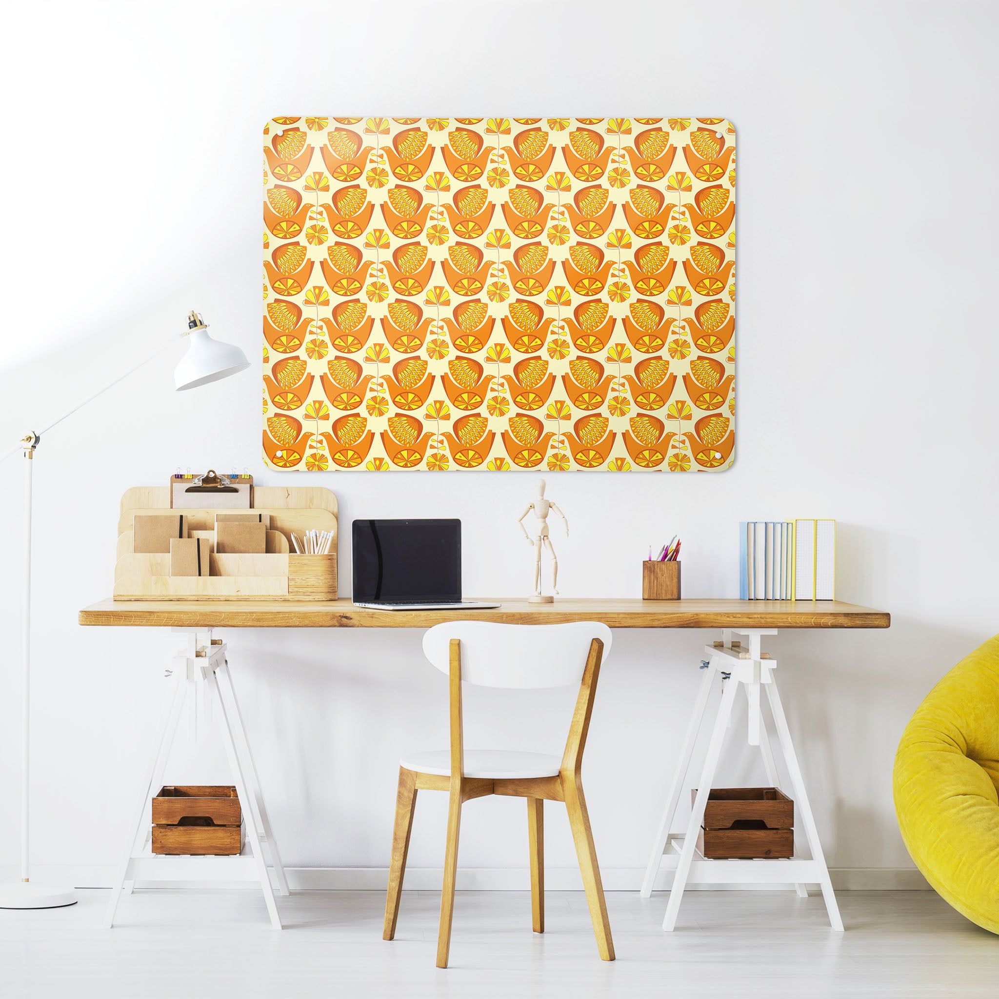A desk in a workspace setting in a white interior with a magnetic metal wall art panel showing a retro citrus bird design in orange and lemon