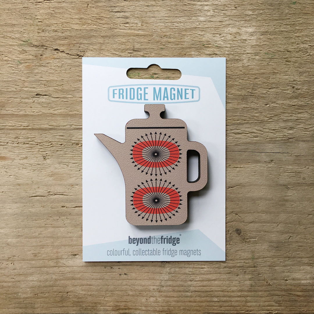 A grey coffee pot shaped plywood fridge magnet by Beyond the Fridge in it’s pack on a wooden background