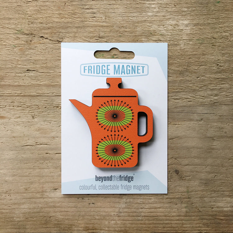 An orange coffee pot shaped plywood fridge magnet by Beyond the Fridge in it’s pack on a wooden background