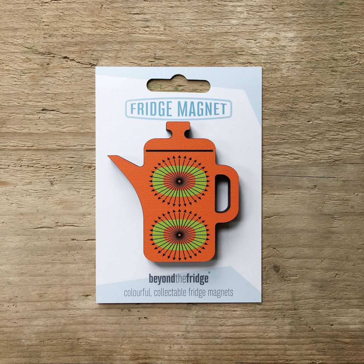 An orange coffee pot shaped plywood fridge magnet by Beyond the Fridge in it’s pack on a wooden background