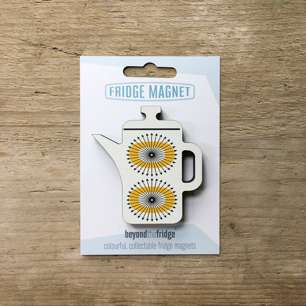 A white coffee pot shaped plywood fridge magnet by Beyond the Fridge in it’s pack on a wooden background