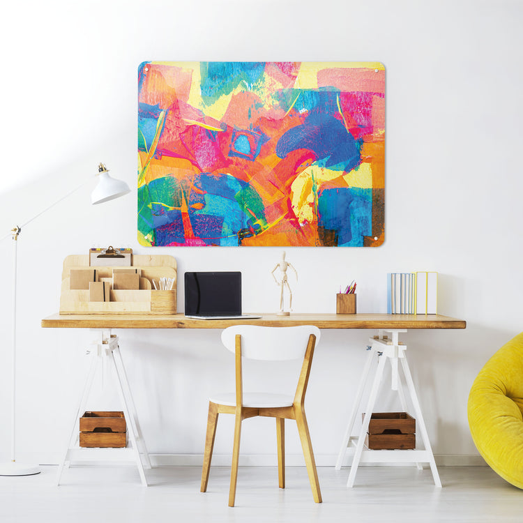 A desk in a workspace setting in a white interior with a magnetic metal wall art panel showing an abstract painting in multi colours called colour pop
