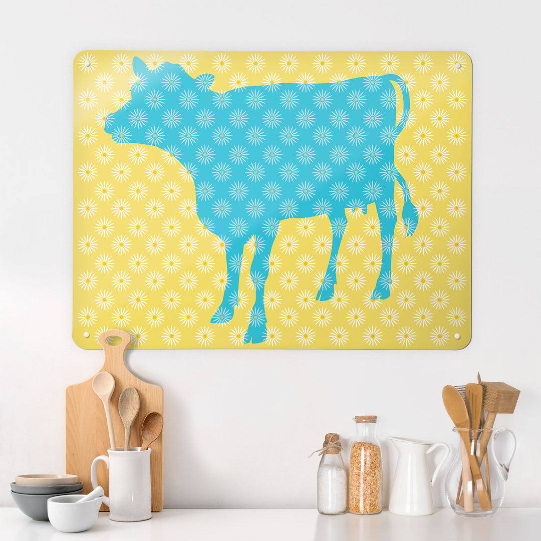 A kitchen interior with a magnetic metal wall art panel showing a daisy the cow design in blue, white and yellow