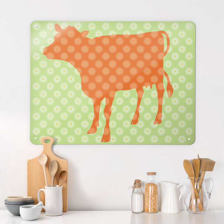 A kitchen interior with a magnetic metal wall art panel showing a daisy the cow design in orange, white and green
