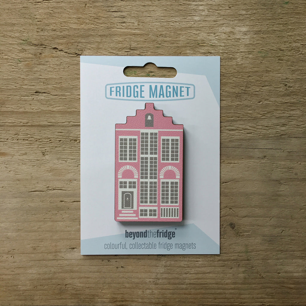 A pink Delft house shaped plywood fridge magnet by Beyond the Fridge in it’s pack on a wooden background