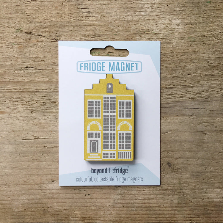 A yellow Delft house shaped plywood fridge magnet by Beyond the Fridge in it’s pack on a wooden background