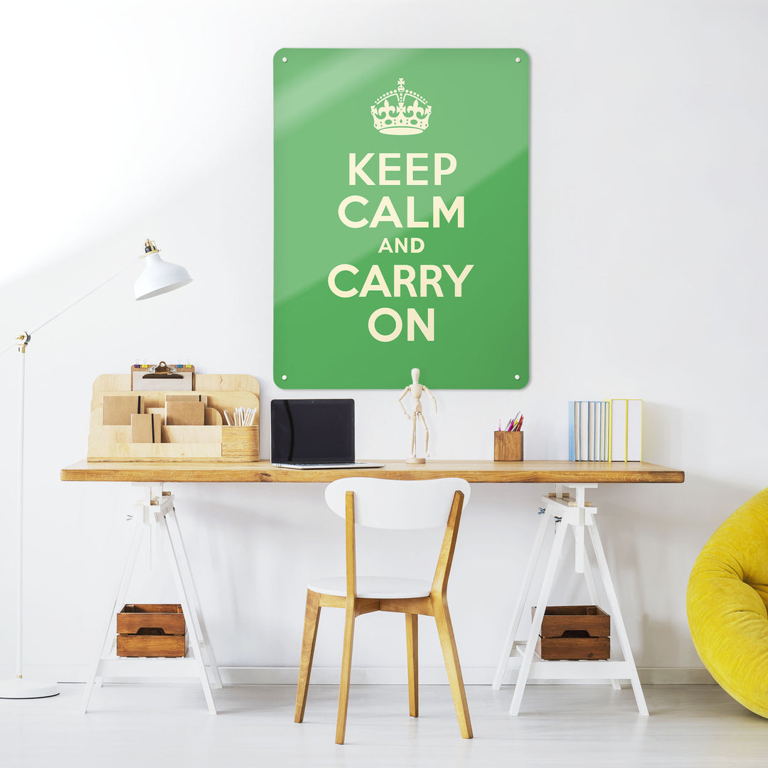 A desk in a workspace setting in a white interior with a magnetic metal wall art panel showing a green vintage keep calm and carry on poster