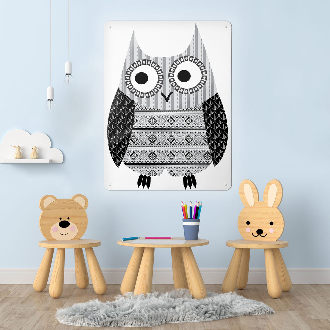 A desk in a playroom  interior with a magnetic metal wall art panel showing a fair isle owl design in black and white