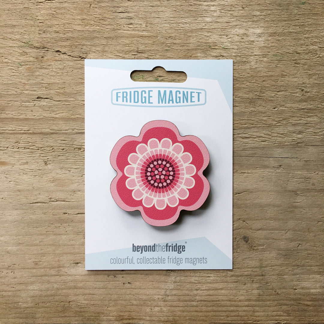 A pink flower design plywood fridge magnet by Beyond the Fridge in it’s pack on a wooden background