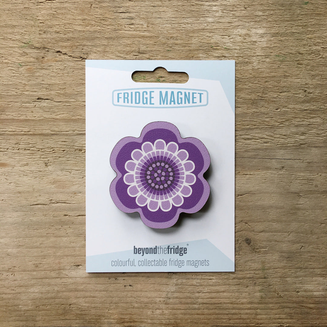 A purple flower design plywood fridge magnet by Beyond the Fridge in it’s pack on a wooden background