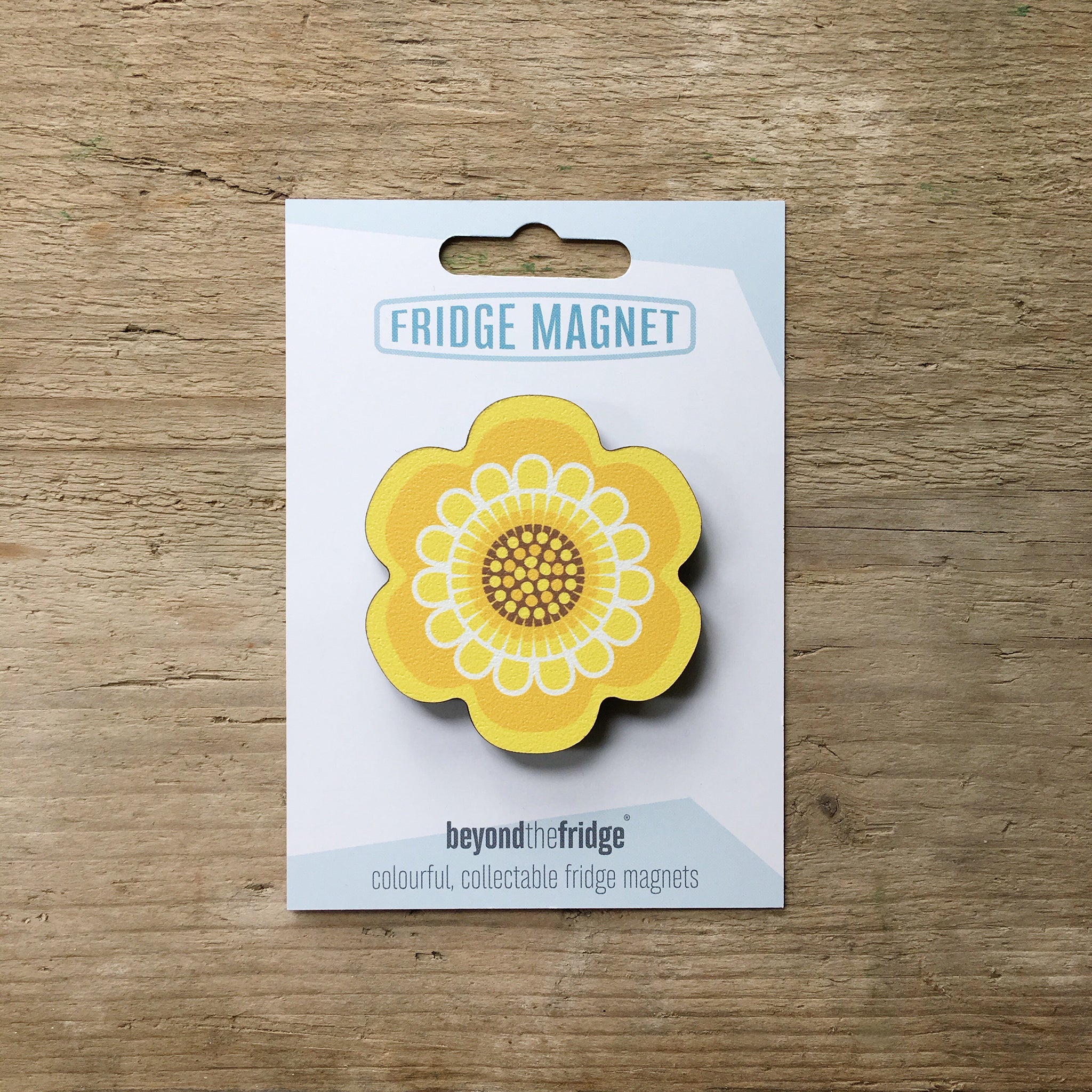 A yellow flower design plywood fridge magnet by Beyond the Fridge in it’s pack on a wooden background