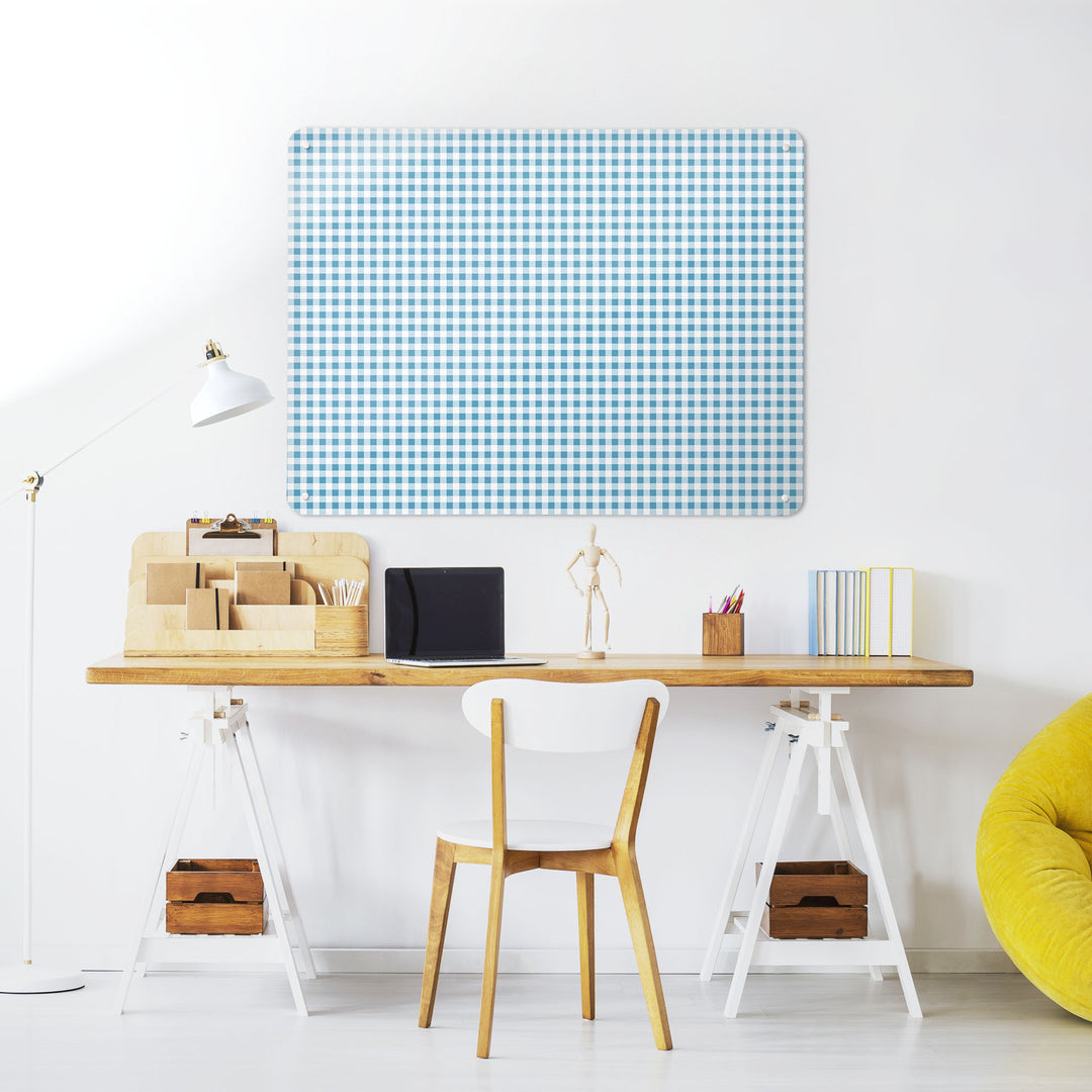 A desk in a workspace setting in a white interior with a magnetic metal wall art panel with a blue gingham design