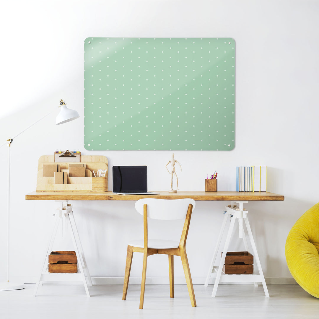A desk in a workspace setting in a white interior with a magnetic metal wall art panel showing a polkadots on green pattern