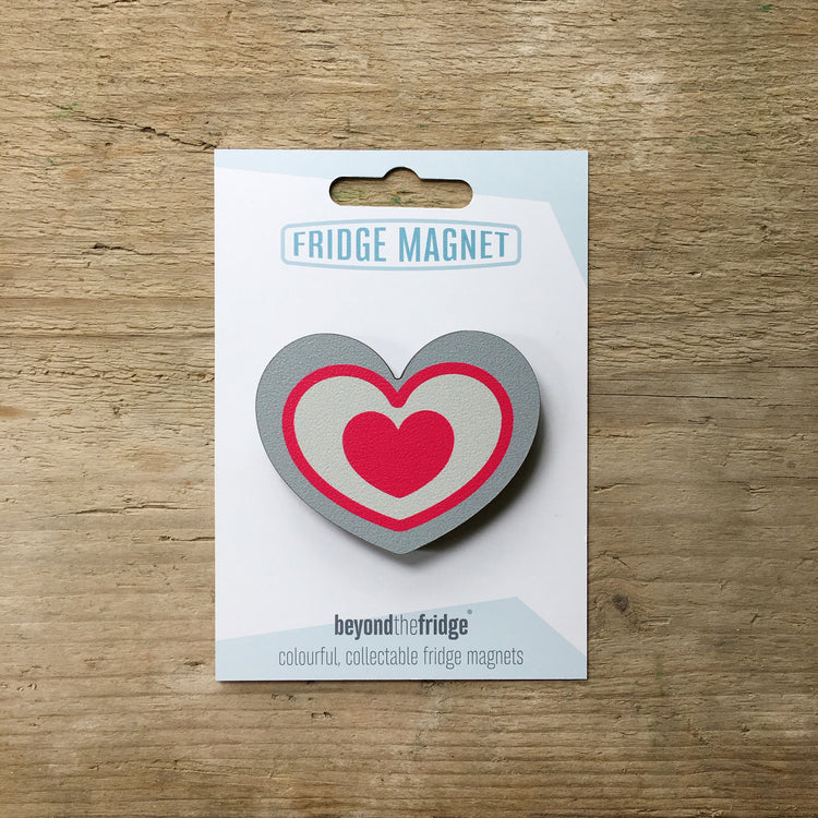 A grey and pink heart design plywood fridge magnet by Beyond the Fridge in it’s pack on a wooden background
