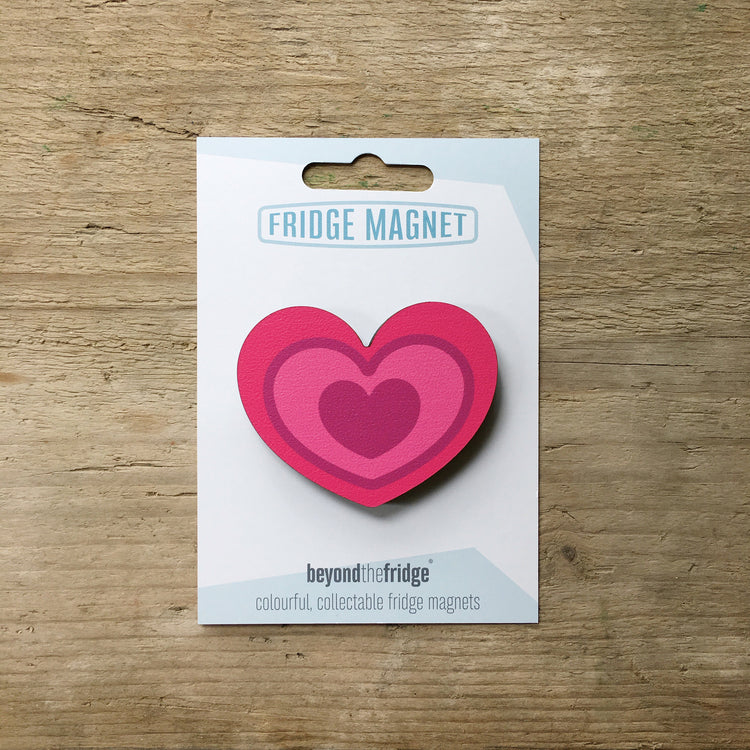 A fuchsia pink heart design plywood fridge magnet by Beyond the Fridge in it’s pack on a wooden background