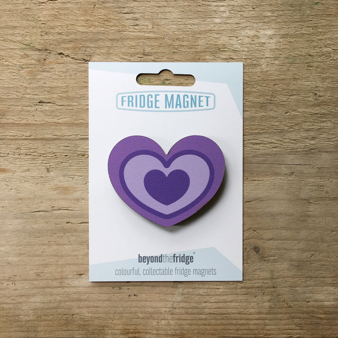 A purple heart design plywood fridge magnet by Beyond the Fridge in it’s pack on a wooden background