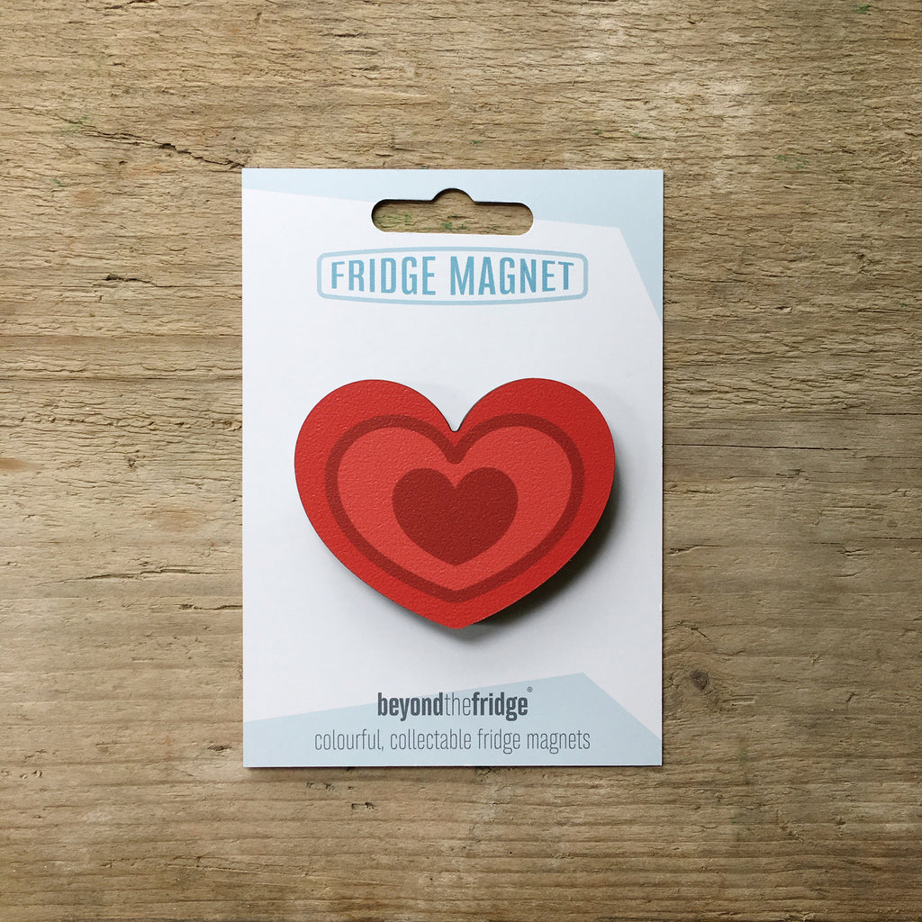 A red heart design plywood fridge magnet by Beyond the Fridge in it’s pack on a wooden background