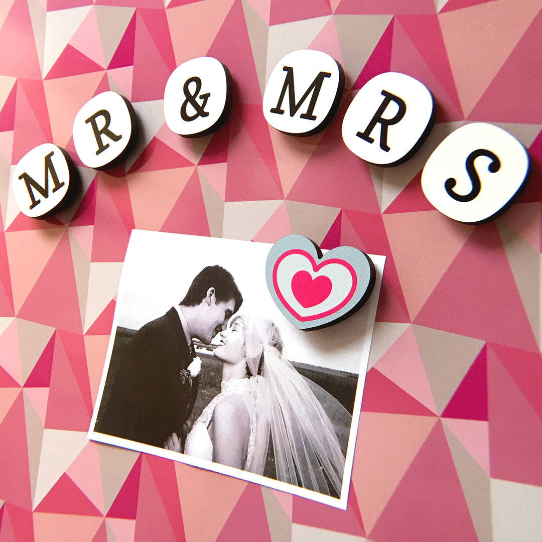 A photograph of a bride and groom attached to a pink magnetic notice with mr & mrs spelt out in fridge magnets with a grey and pink heart shaped magnet