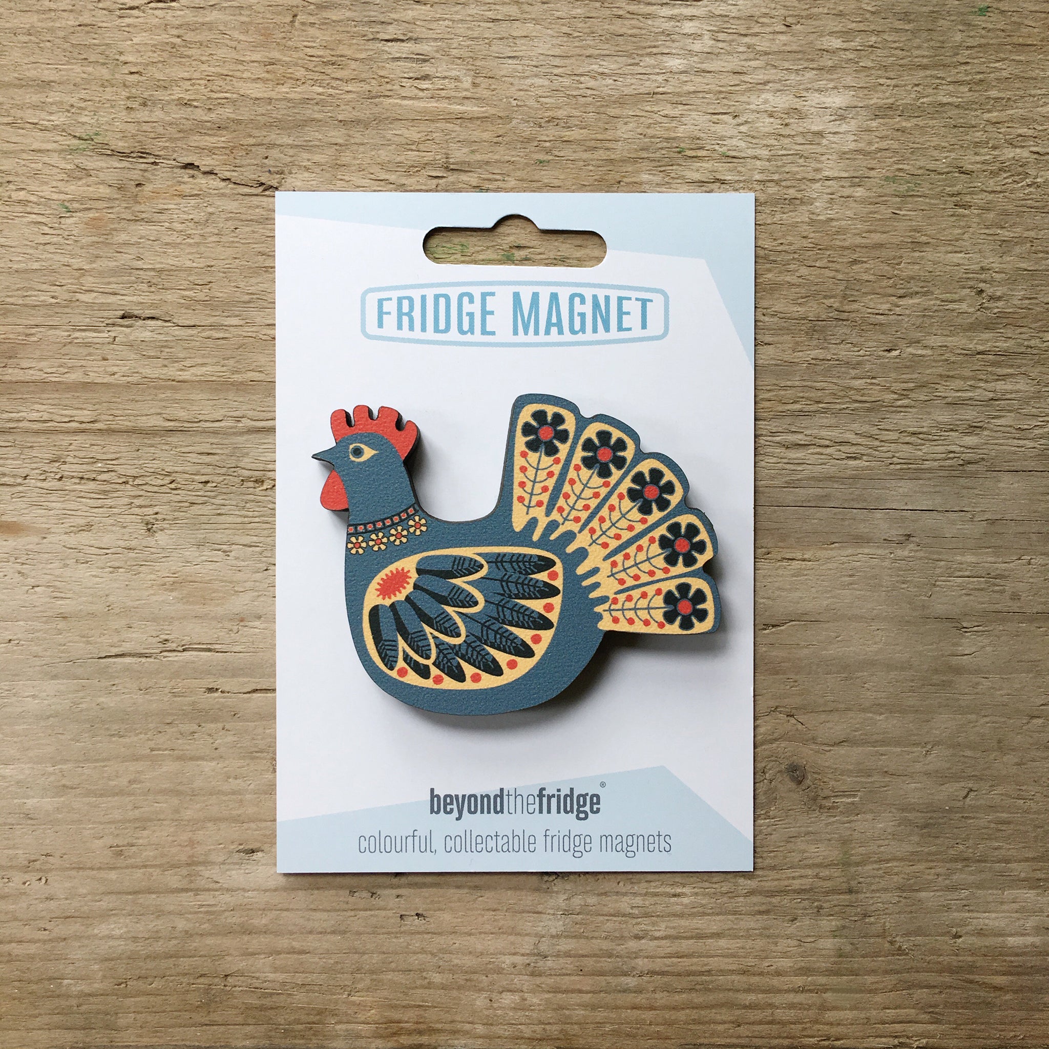 A blue hen design plywood fridge magnet by Beyond the Fridge in it’s pack on a wooden background