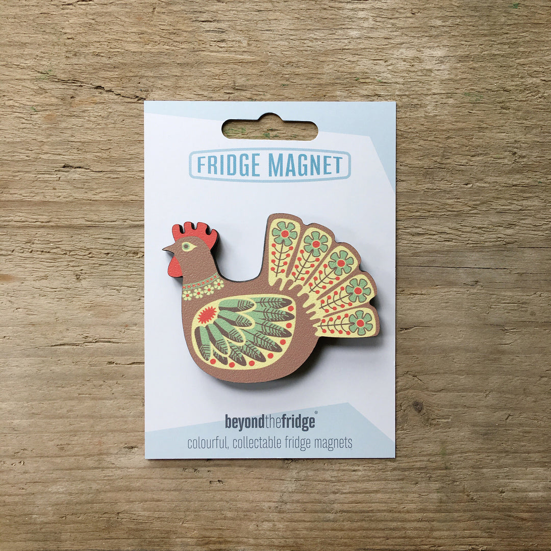 A brown hen design plywood fridge magnet by Beyond the Fridge in it’s pack on a wooden background