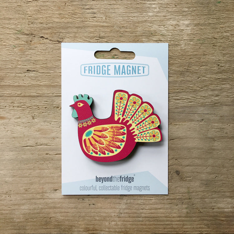 A red hen design plywood fridge magnet by Beyond the Fridge in it’s pack on a wooden background