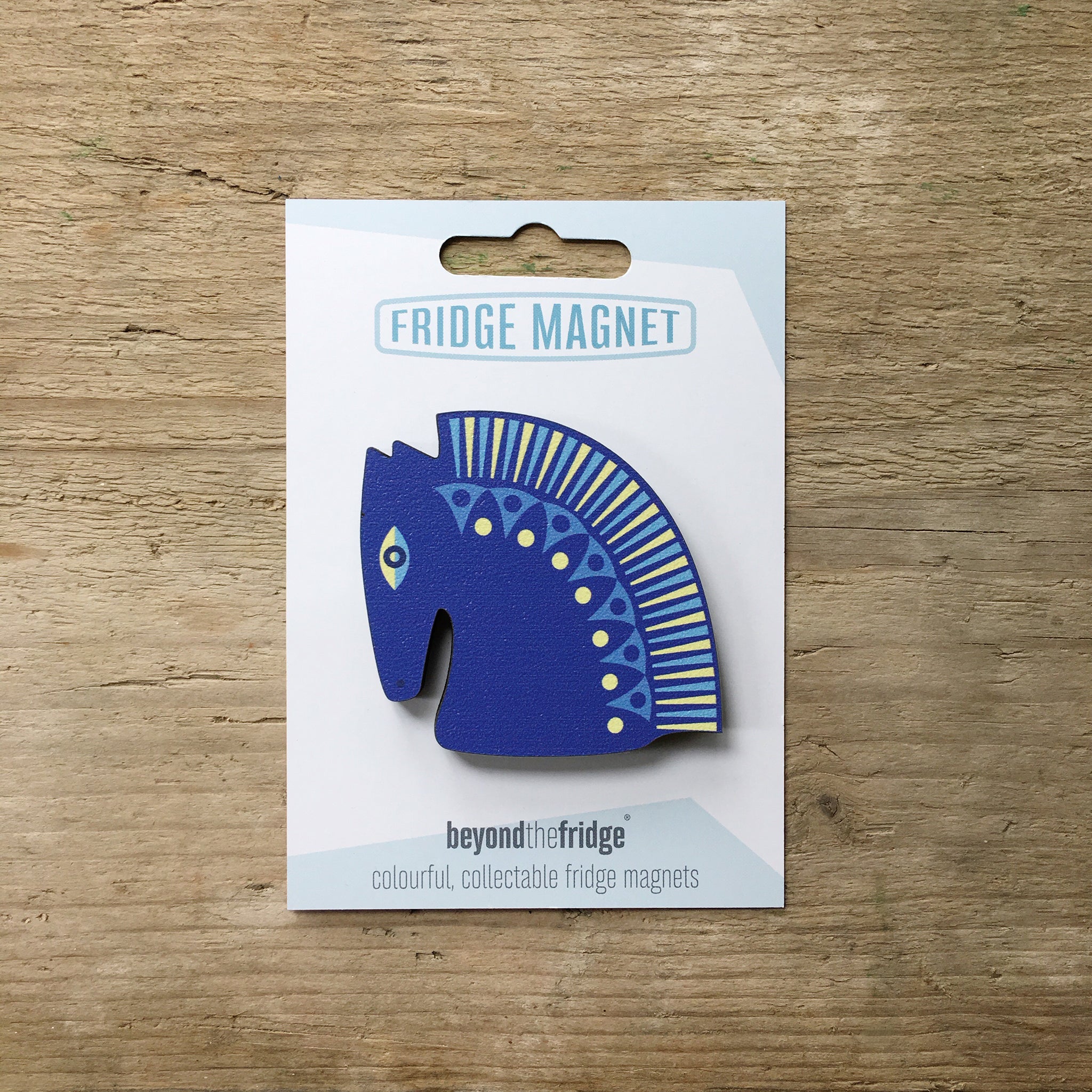 A blue horse head design plywood fridge magnet by Beyond the Fridge in it’s pack on a wooden background