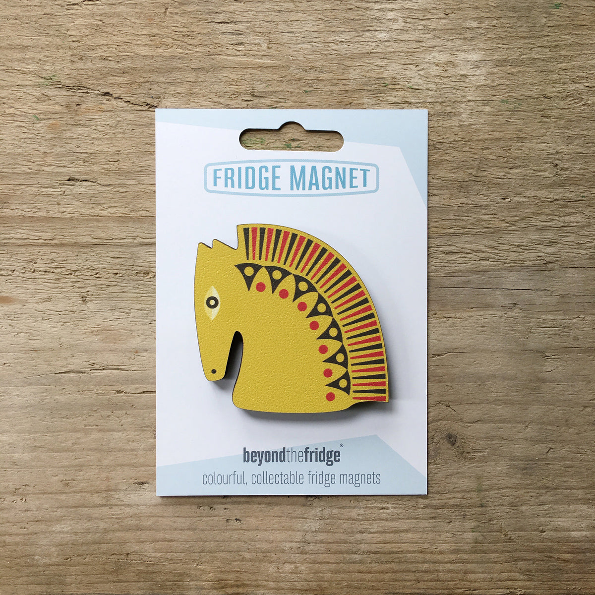 A mustard horse head design plywood fridge magnet by Beyond the Fridge in it’s pack on a wooden background