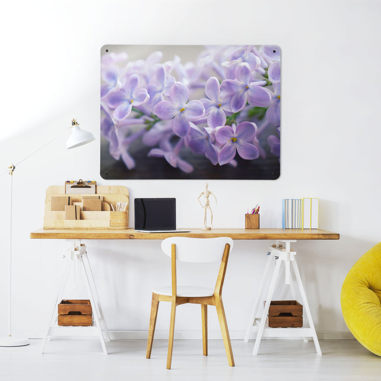 A desk in a workspace setting in a white interior with a magnetic metal wall art panel showing a photograph of lilac flowers