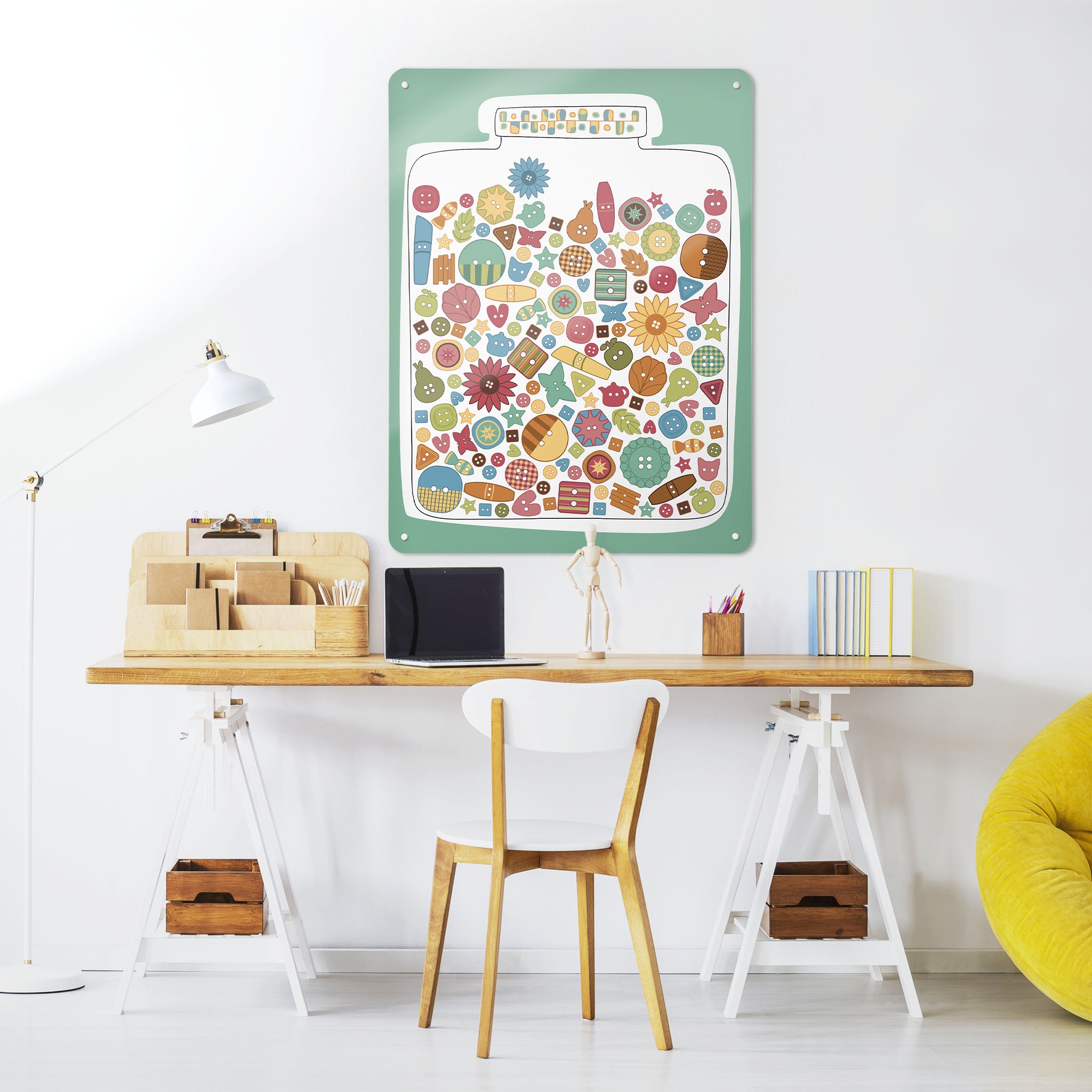 A desk in a workspace setting in a white interior with a magnetic metal wall art panel showing a jar full of multi coloured buttons design