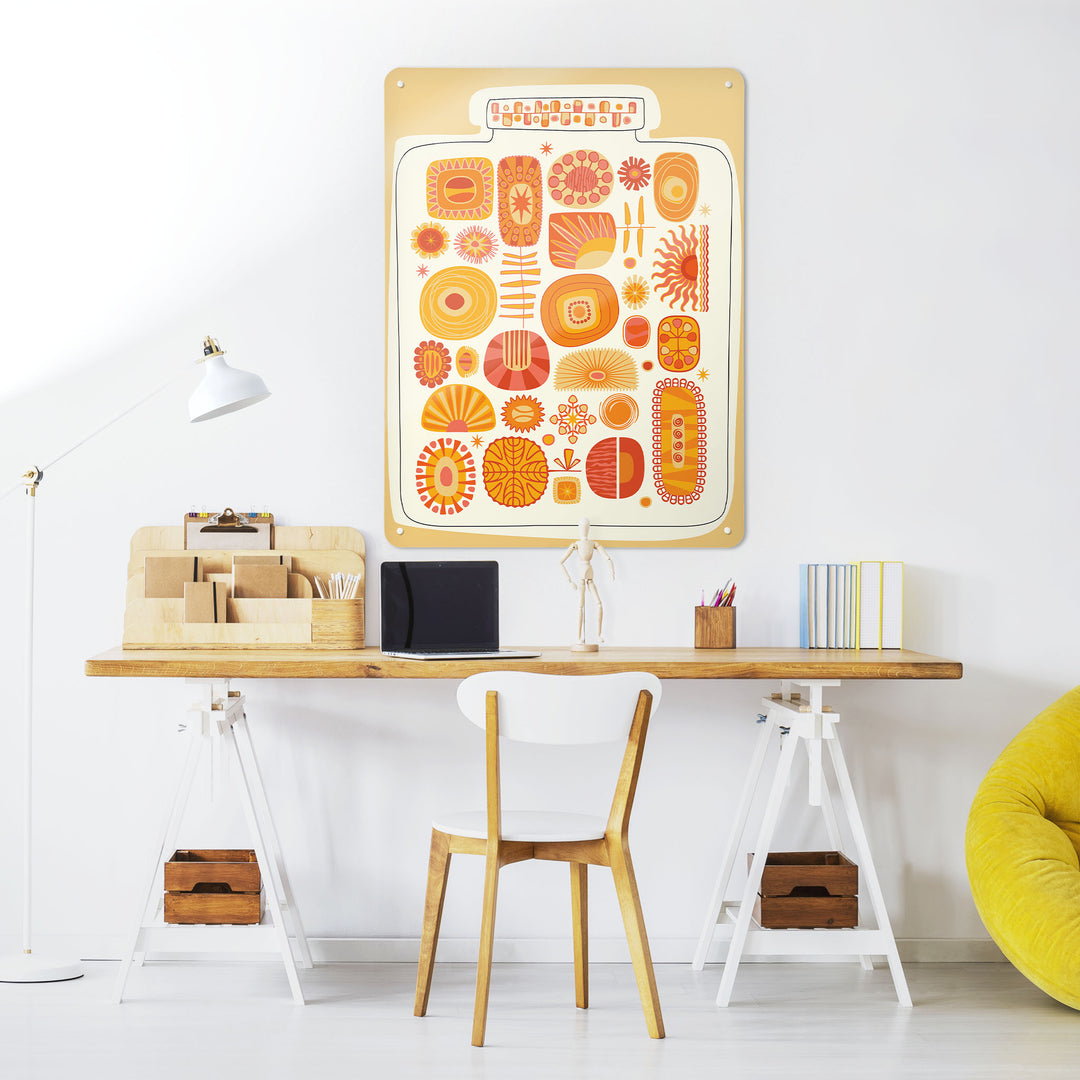 A desk in a workspace setting in a white interior with a magnetic metal wall art panel showing a jar full of orange and yellow suns design