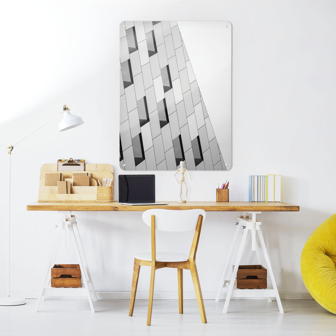 A desk in a workspace setting in a white interior with a magnetic metal wall art panel showing A desk in a workspace setting in a white interior with a magnetic metal wall art panel showing an abstract image of windows on a modern building