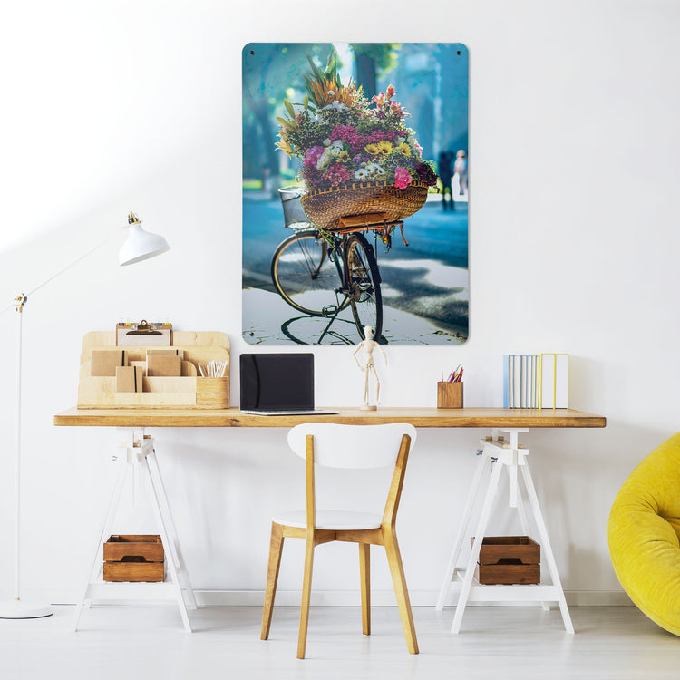 A desk in a workspace setting in a white interior with a magnetic metal wall art panel showing a photograph of a bicycle with a large basket of flowers
