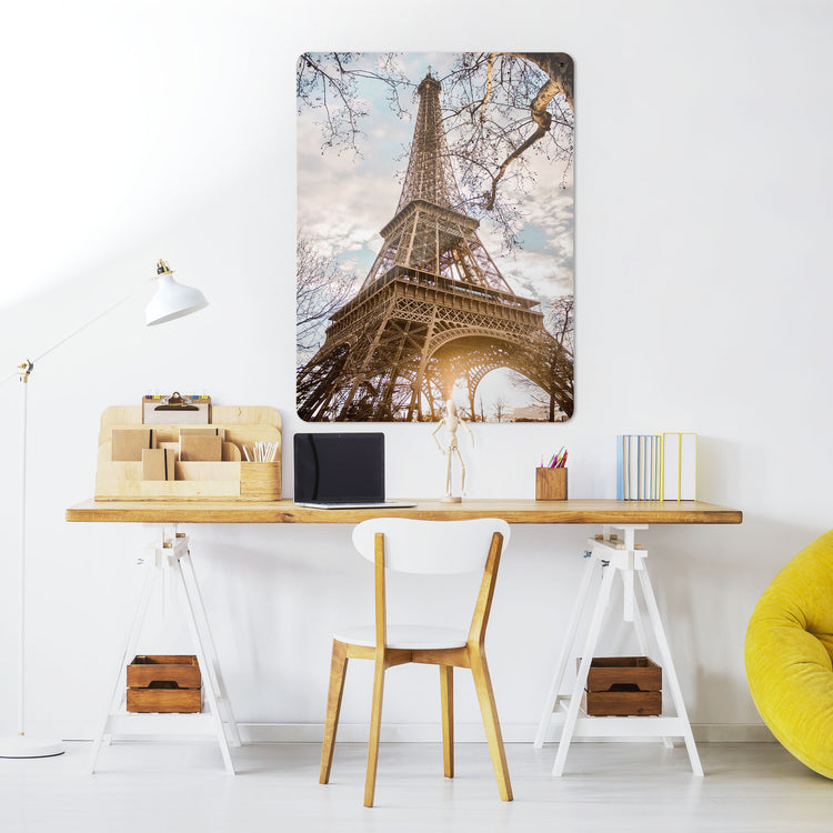 A desk in a workspace setting in a white interior with a magnetic metal wall art panel showing a photograph of the Eiffel Tower