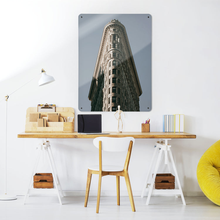 A desk in a workspace setting in a white interior with a magnetic metal wall art panel showing the Flatiron Building in Manhattan