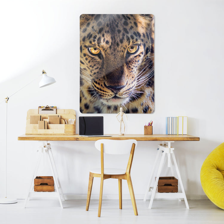 A desk in a workspace setting in a white interior with a magnetic metal wall art panel showing a close up photograph of the face of a leopard