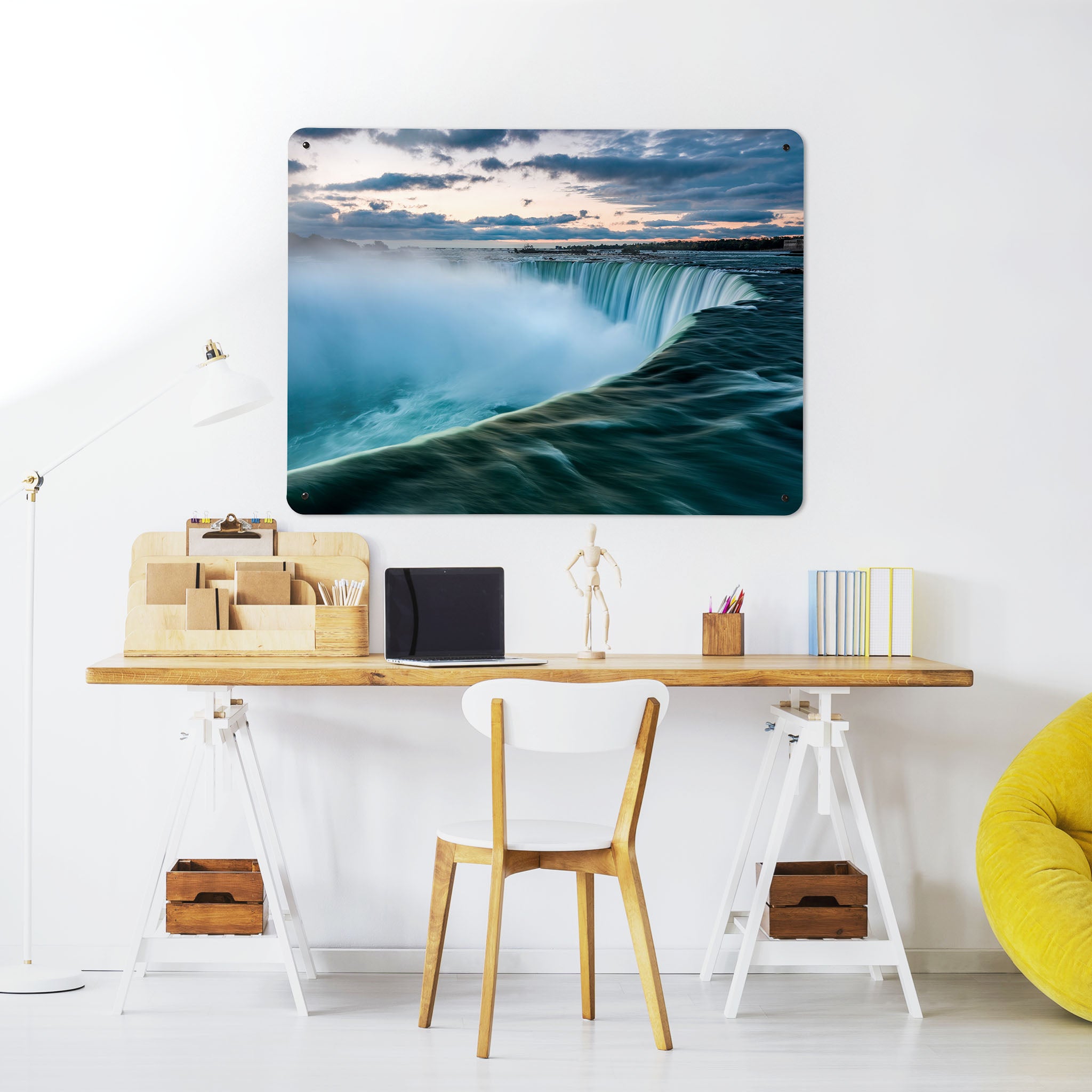A desk in a workspace setting in a white interior with a magnetic metal wall art panel showing a photograph of the Niagara Falls