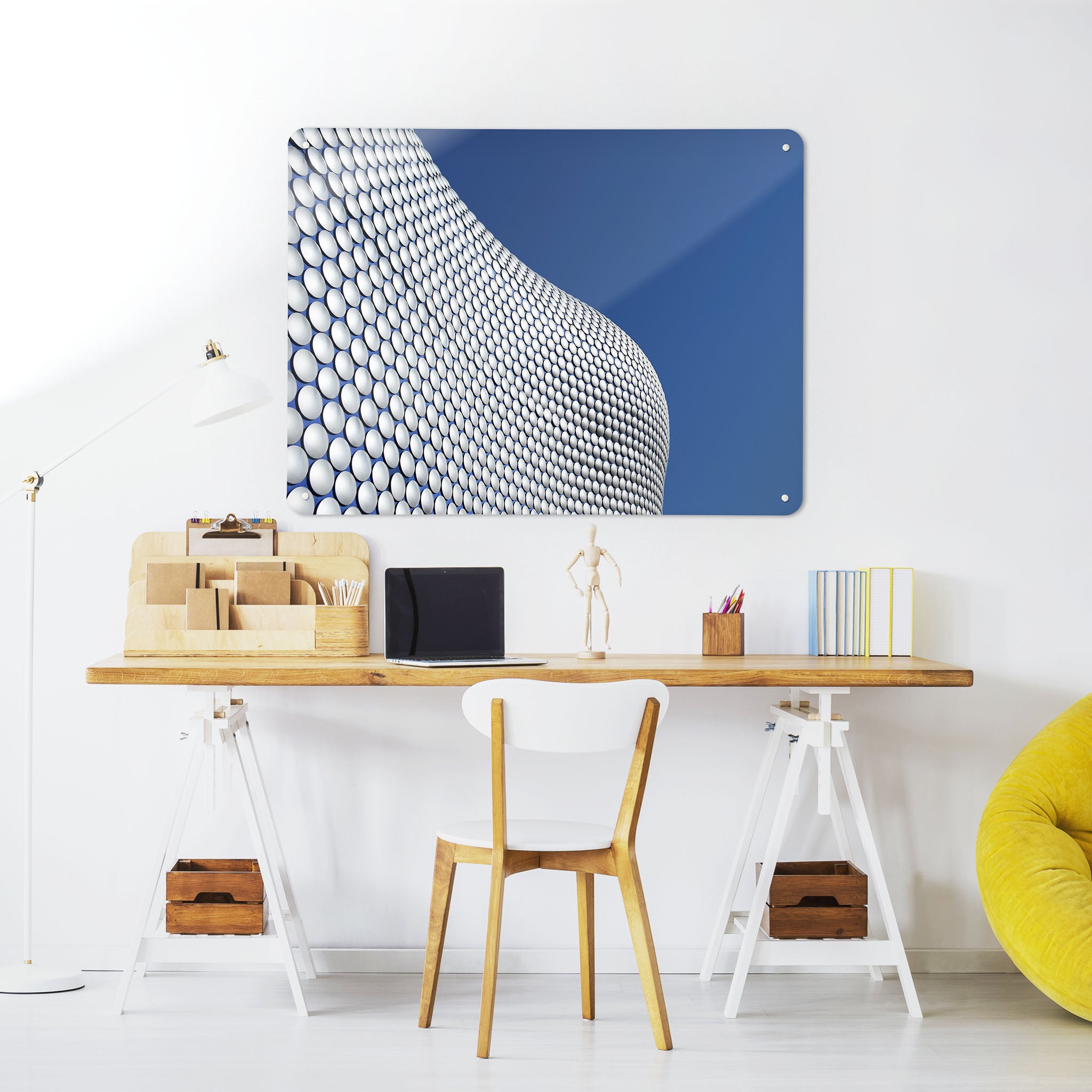 A desk in a workspace setting in a white interior with a magnetic metal wall art panel showing a photograph of the Selfridges Building Birmingham