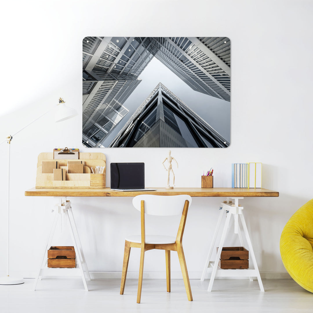 A desk in a workspace setting in a white interior with a magnetic metal wall art panel showing a dramatic photographic image of Zürich Skyscrapers