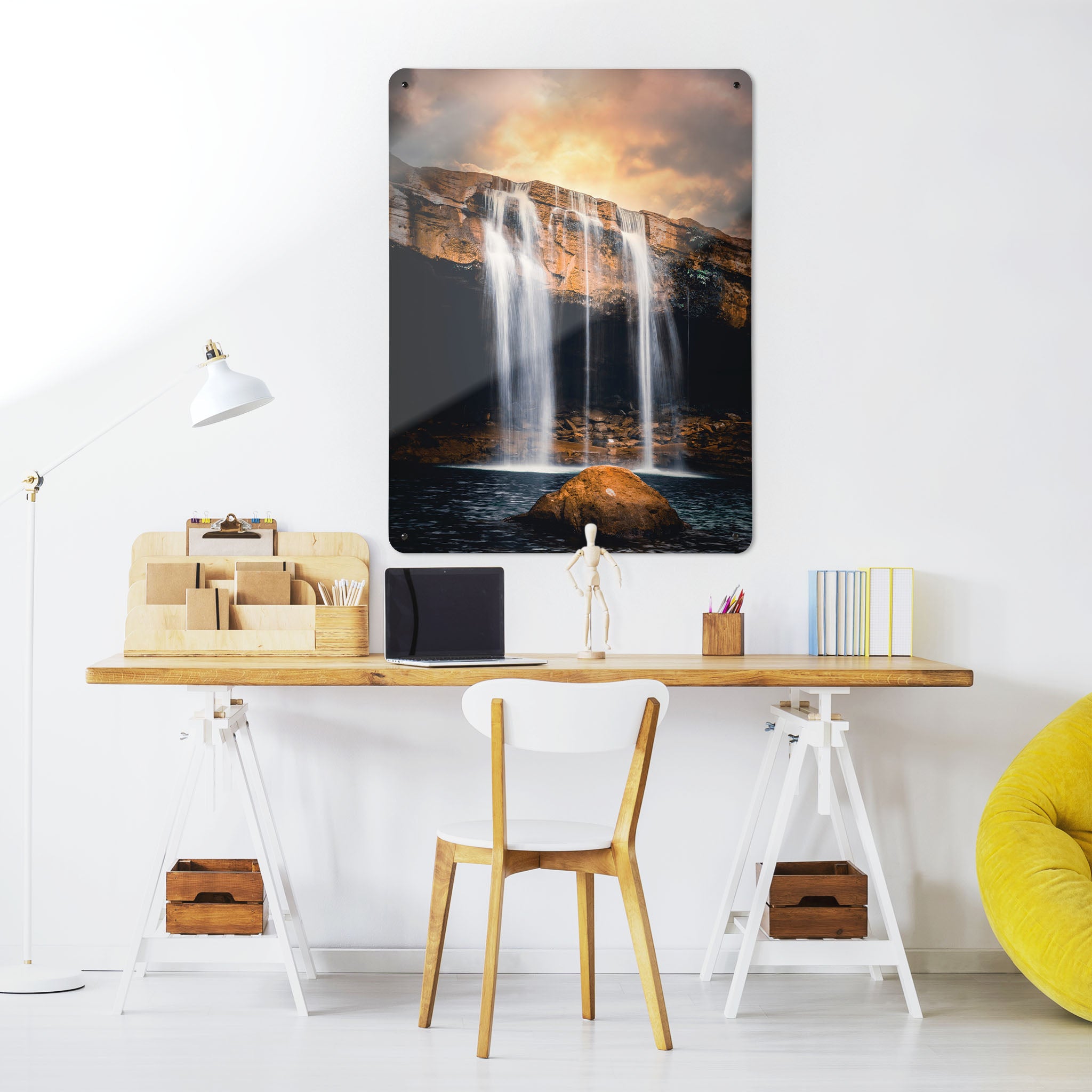 A desk in a workspace setting in a white interior with a magnetic metal wall art panel showing a waterfall at sunset