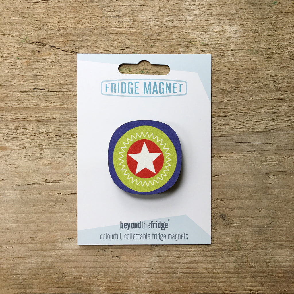 A white star millefiori design plywood fridge magnet by Beyond the Fridge in it’s pack on a wooden background