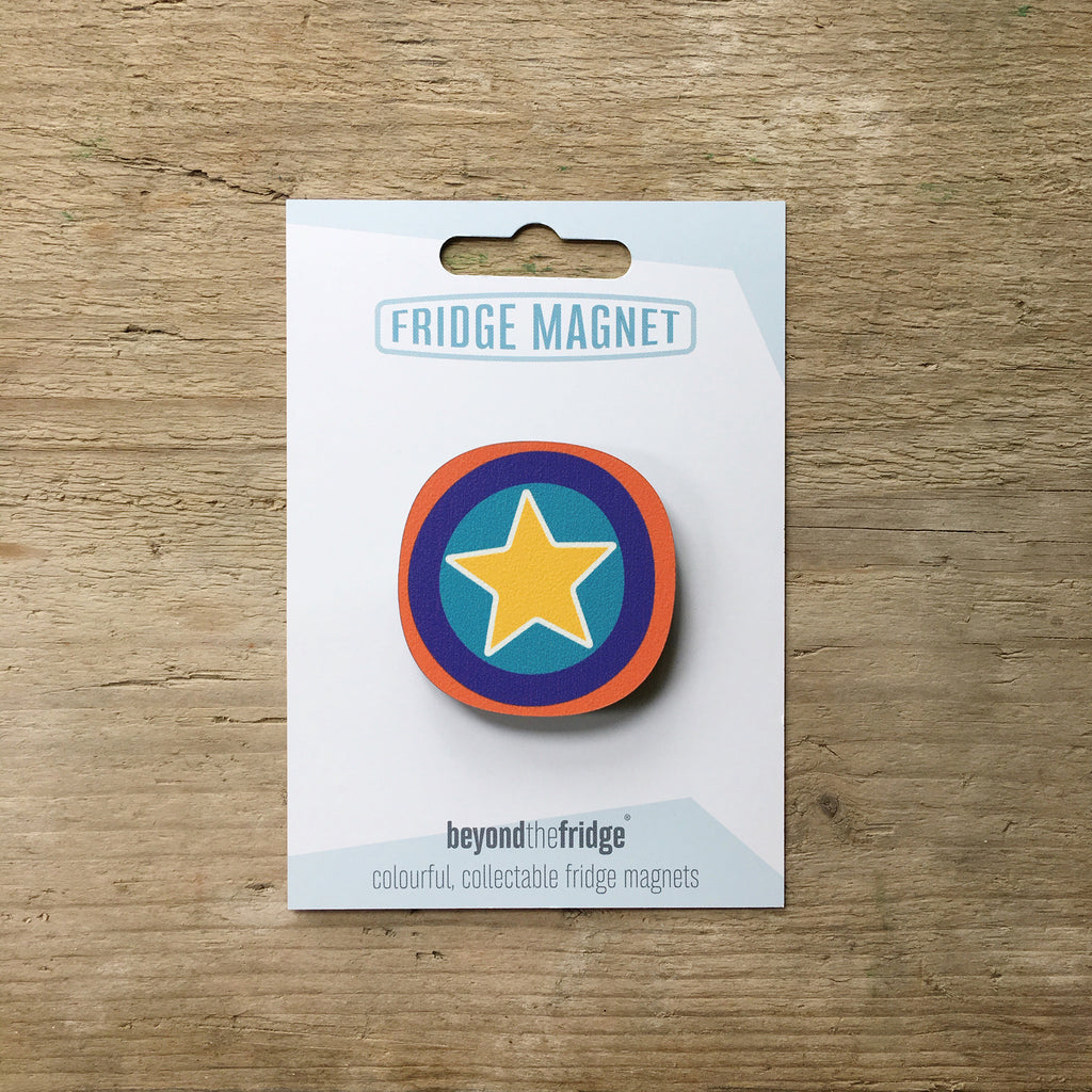A yellow star millefiori design plywood fridge magnet by Beyond the Fridge in it’s pack on a wooden background