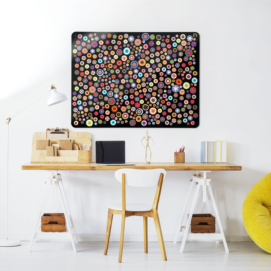 A desk in a workspace setting in a white interior with a magnetic metal wall art panel showing millefiori pattern on a black background