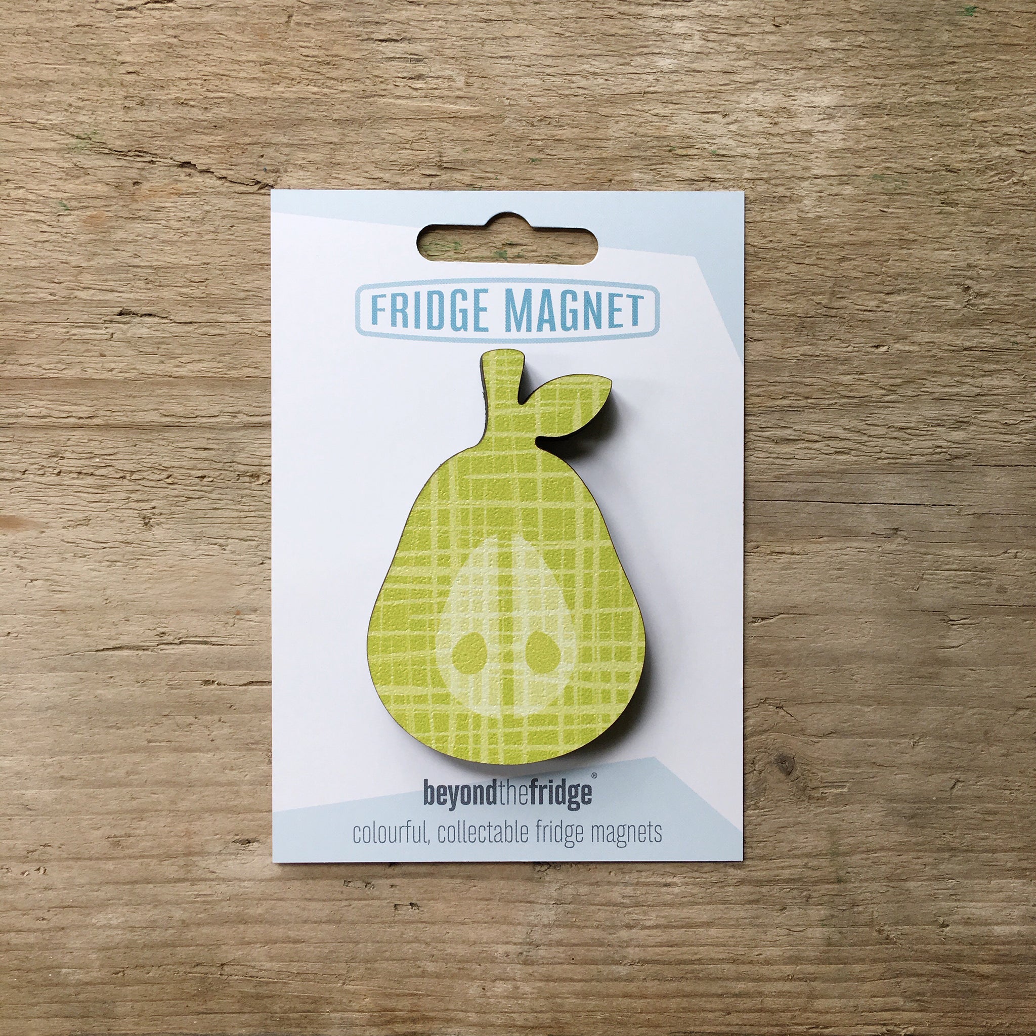 A green pear design plywood fridge magnet by Beyond the Fridge in it’s pack on a wooden background