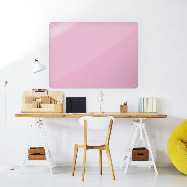 A desk in a workspace setting in a white interior with a plain pink coloured magnetic metal wall art panel 
