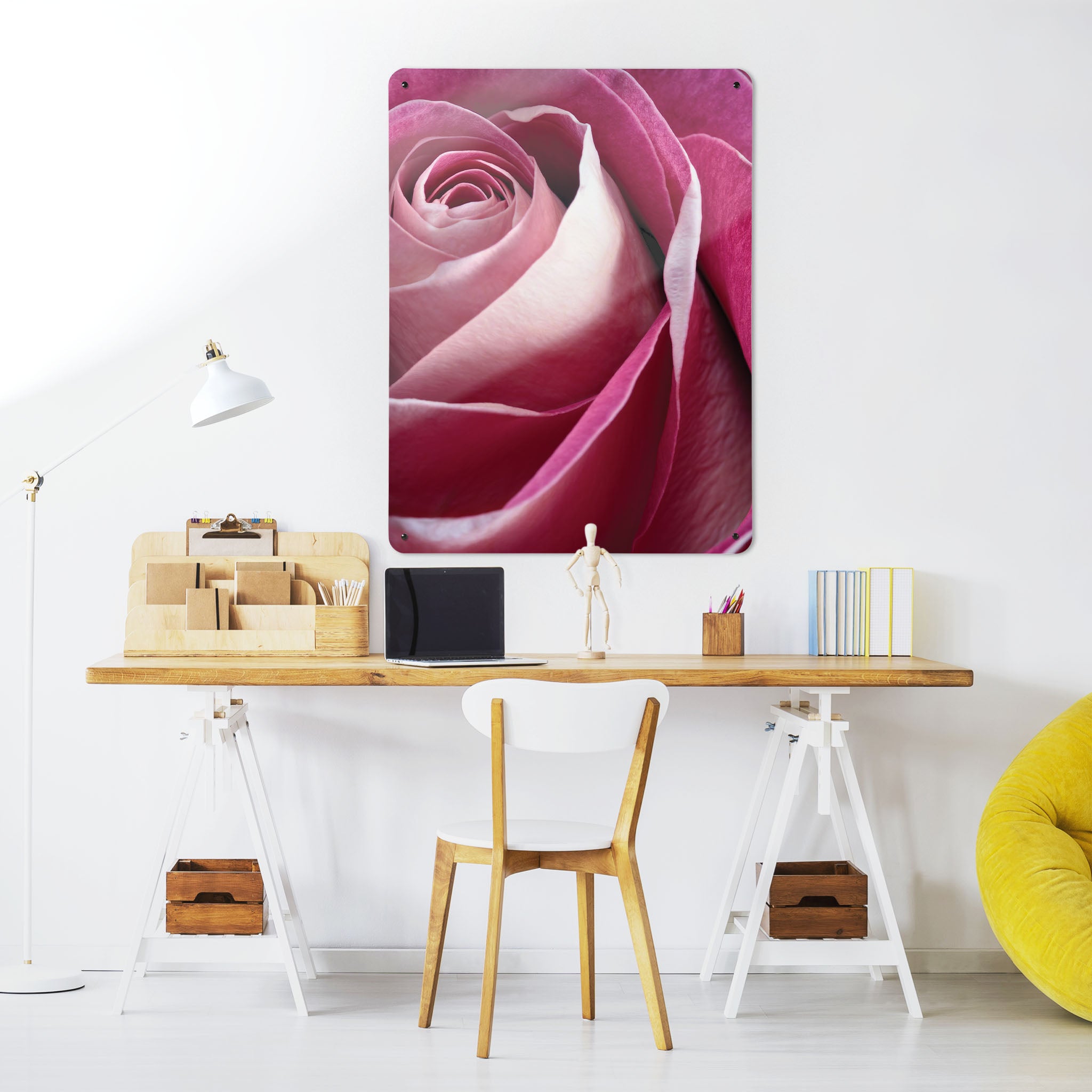 A desk in a workspace setting in a white interior with a magnetic metal wall art panel showing a photographic image of a pink rose