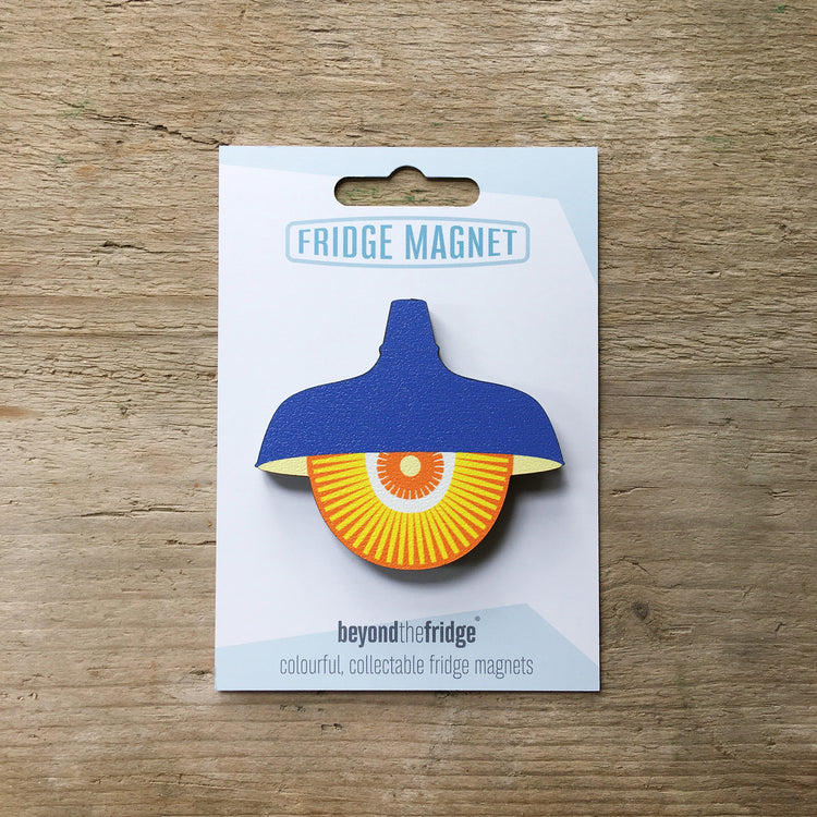A blue retro pendant light design plywood fridge magnet by Beyond the Fridge in it’s pack on a wooden background