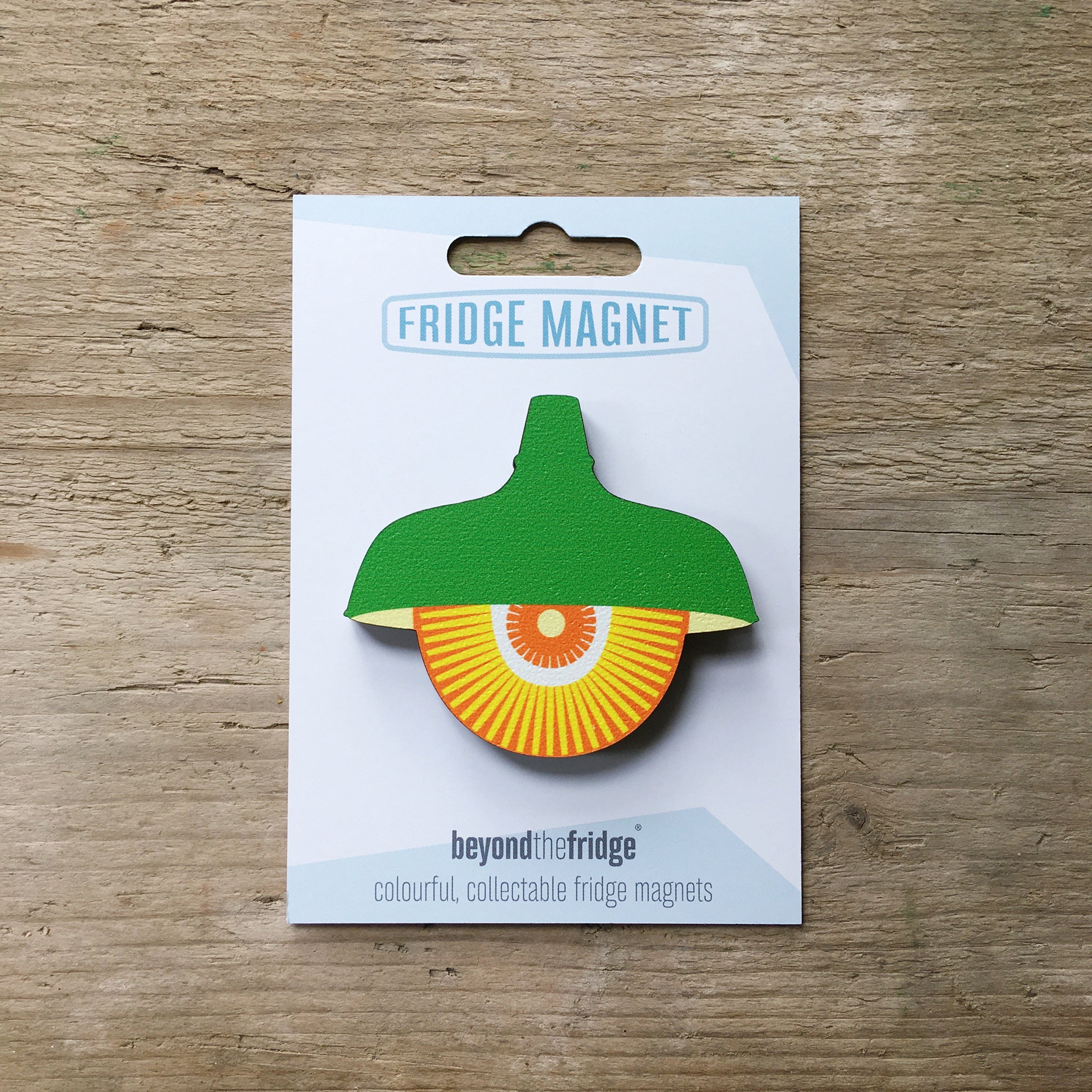 A green retro pendant light design plywood fridge magnet by Beyond the Fridge in it’s pack on a wooden background