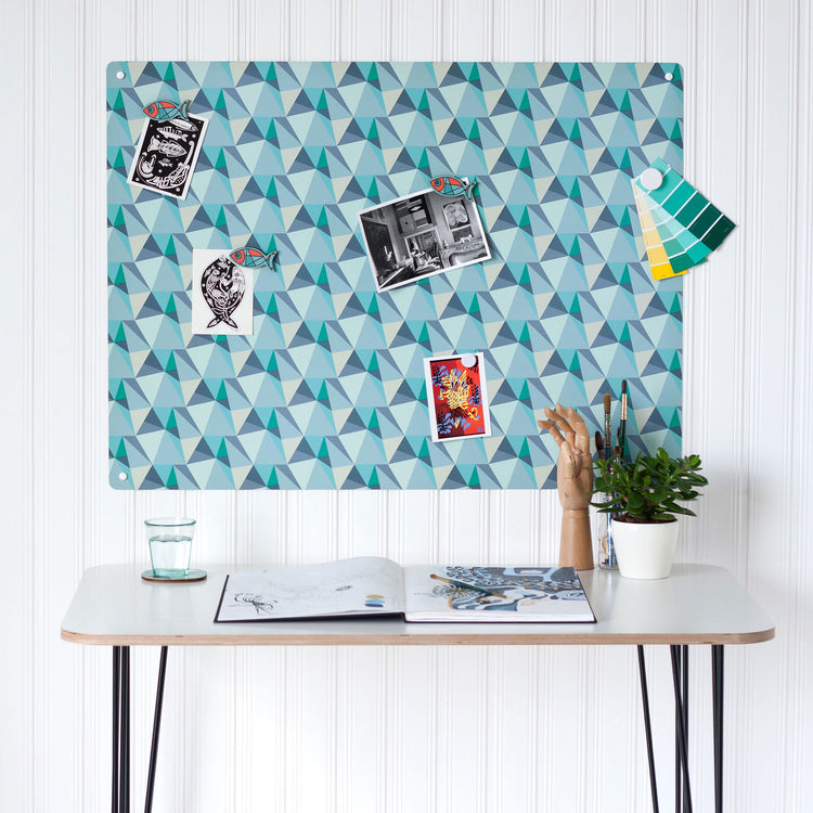 A desk in a workspace setting in a white interior with a magnetic metal wall art panel showing a shards design in ocean colour way