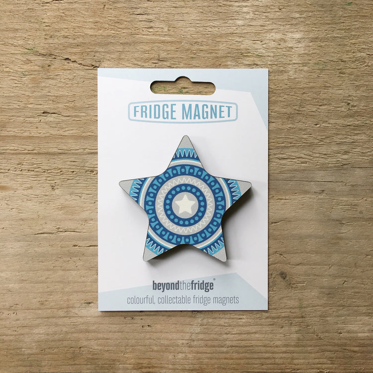 A blue star design plywood fridge magnet by Beyond the Fridge in it’s pack on a wooden background