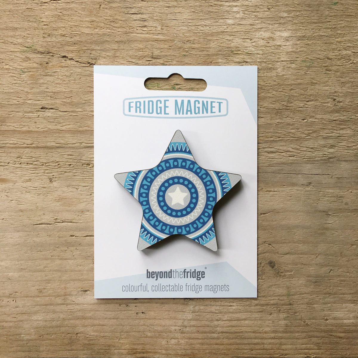 A blue star design plywood fridge magnet by Beyond the Fridge in it’s pack on a wooden background
